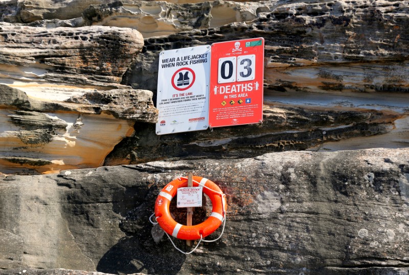 © Reuters. A sign warning rock fishermen of the dangers of the surf sits attached to a rock face above a floatation device in the Sydney suburb of Maroubra