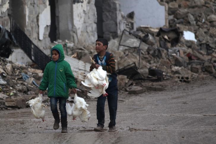 © Reuters. Crianças passam por prédios destruídos carregando galinhas em al-Rai, ao norte de Aleppo, na Síria