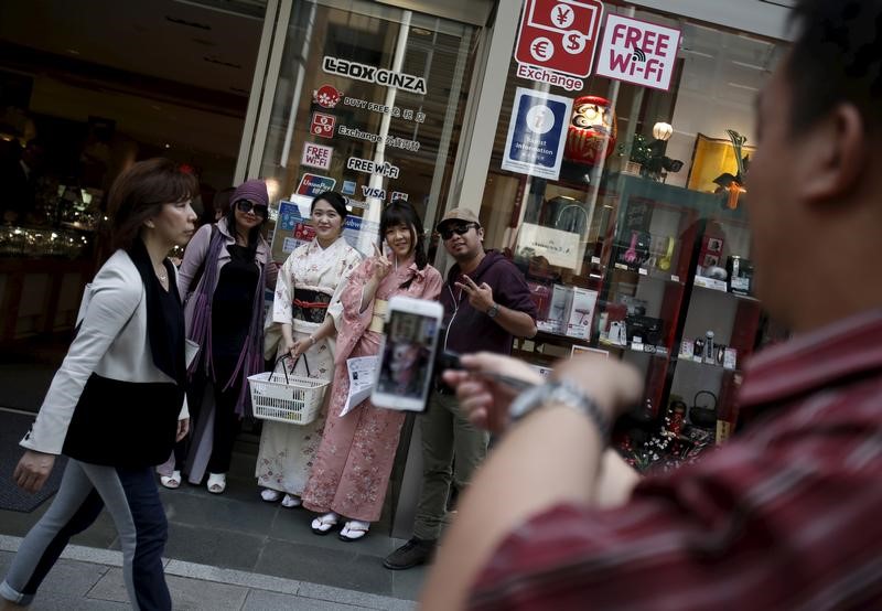 © Reuters. Foreign tourists pose with shop clerks for pictures outside a duty free store at Ginza shopping district in Tokyo