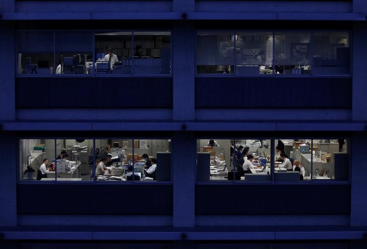 © Reuters. Office workers are pictured through building windows during dusk in Tokyo