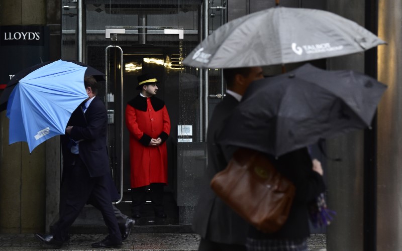 © Reuters. A doorman looks out as workers walk in the rain past the Lloyd's of London building in the City of London