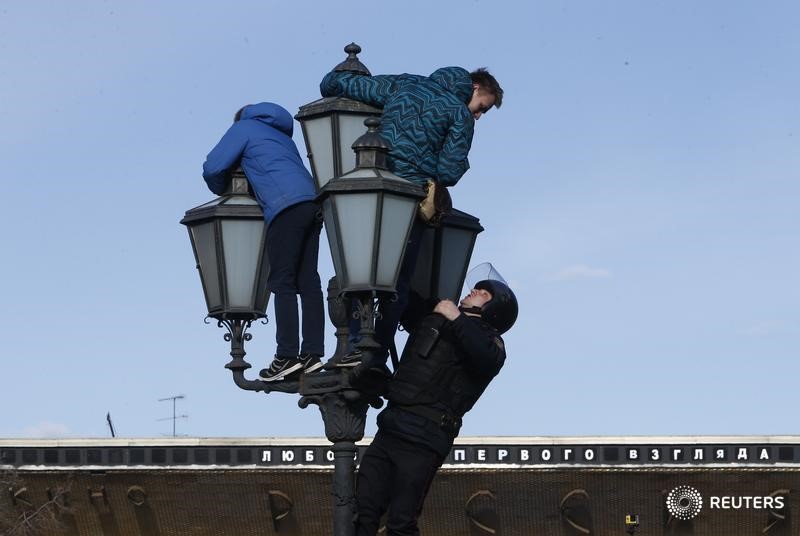 © Reuters. Сотрудник полиции пытается снять людей с фонарного столба во время акции протеста в Москве