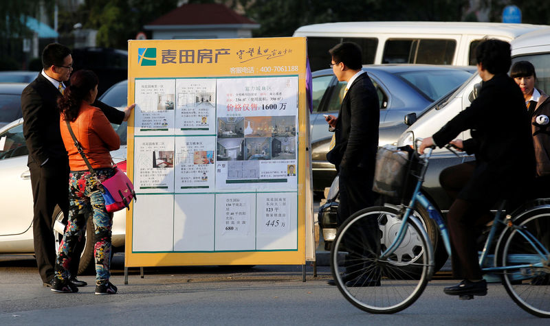 © Reuters. FILE PHOTO: A real estate agent introduces apartment information on a board to a woman along a street in Beijing