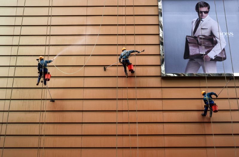 © Reuters. Workers clean exteriors of a building next to an advertisement in Wuxi