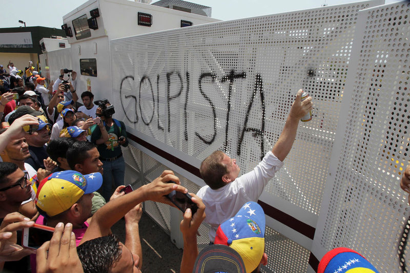 © Reuters. A man spray paints a graffiti that reads "coup" on an anti-riot barricade during a rally against Venezuela's President Nicolas Maduro's government in Maracaibo, Venezuela