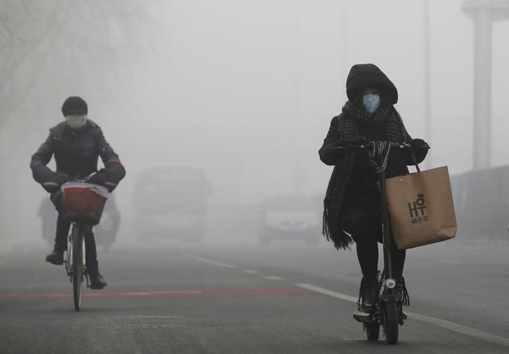 © Reuters. Pessoas andam de bicicleta em meio a fumaça em Pequim, na China.