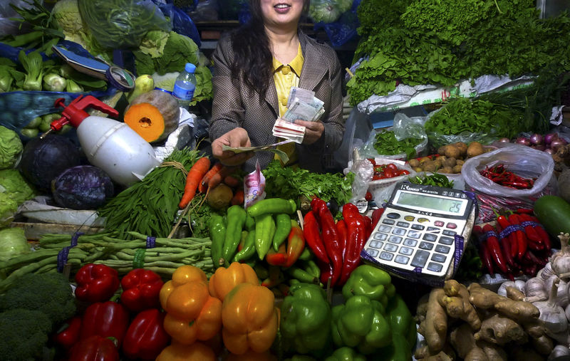 © Reuters. FILE PHOTO: A fruit and vegetable stall owner uses a calculator to work out prices for a customer at a small market in central Beijing, China