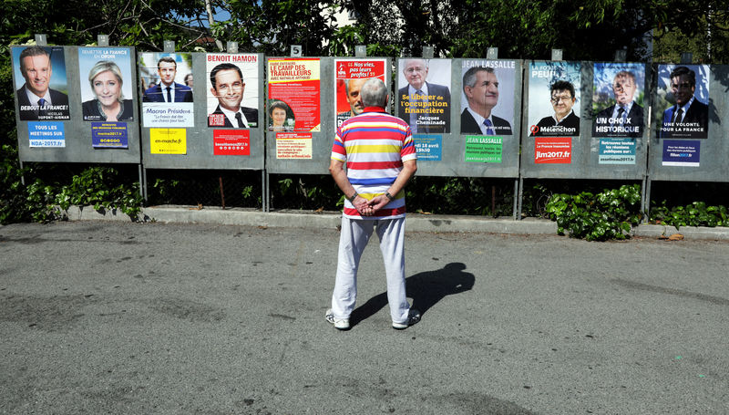 © Reuters. FILE PHOTO: A man looks at campaign posters of the 11th candidates who run in the 2017 French presidential election in Saint Andre de La Roche