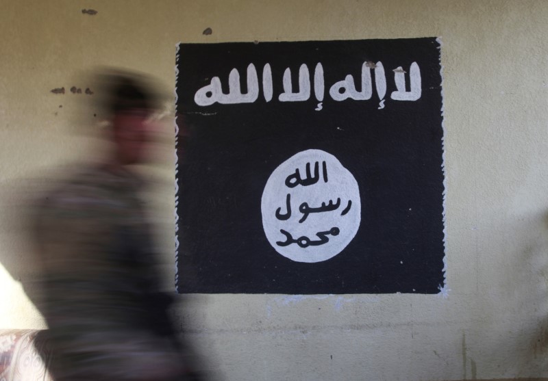 © Reuters. A member of the Iraqi rapid response forces walks past a wall painted with the black flag commonly used by Islamic State militants, during battle in the Wahda district of eastern Mosul, Iraq