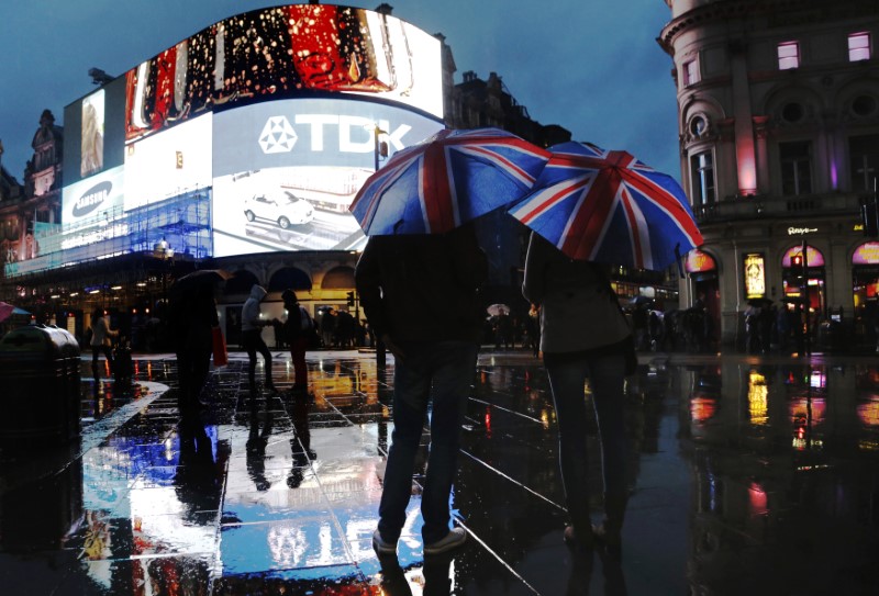 © Reuters. People stand under Union Flag umbrellas during rain in Piccadilly Circus in London