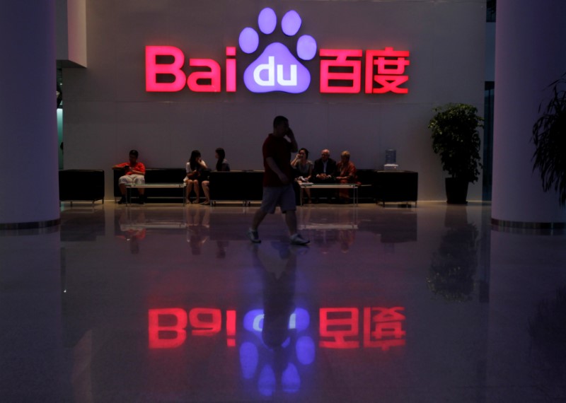 © Reuters. A employee uses his mobile phone as he walks past the company logo of Baidu at its headquarters in Beijing