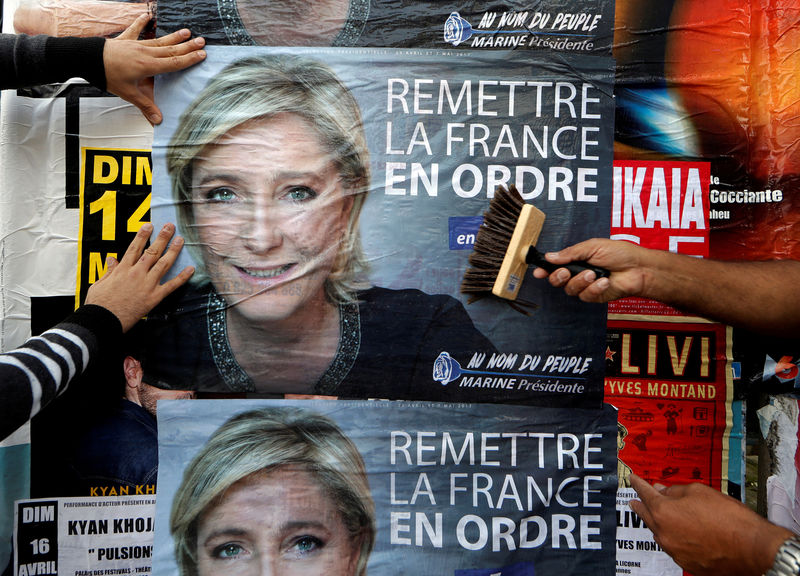 © Reuters. FILE PHOTO: Members of the French National Front (FN) political party paste a poster on a free billboard for the French National Front political party leader Marine Le Pen in Antibes