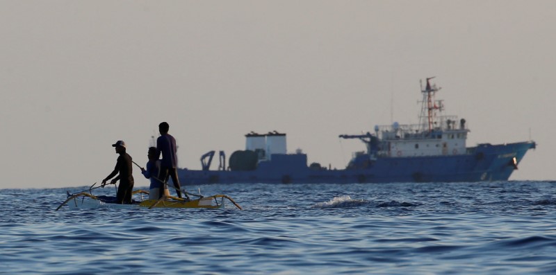 © Reuters. Filipino fishermen past a large Chinese vessel at the disputed Scarborough Shoal