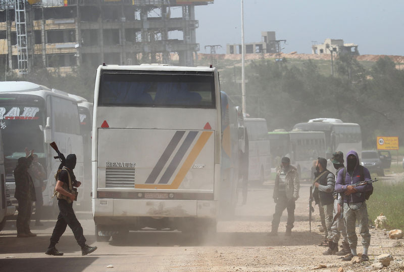 © Reuters. Rebel fighters stand guard as a convoy of buses carrying Sunni rebels and civilians, who were evacuated from Zabadani and Madaya, as part of a reciprocal evacuation deal for four besieged towns, travel in al-Rashideen