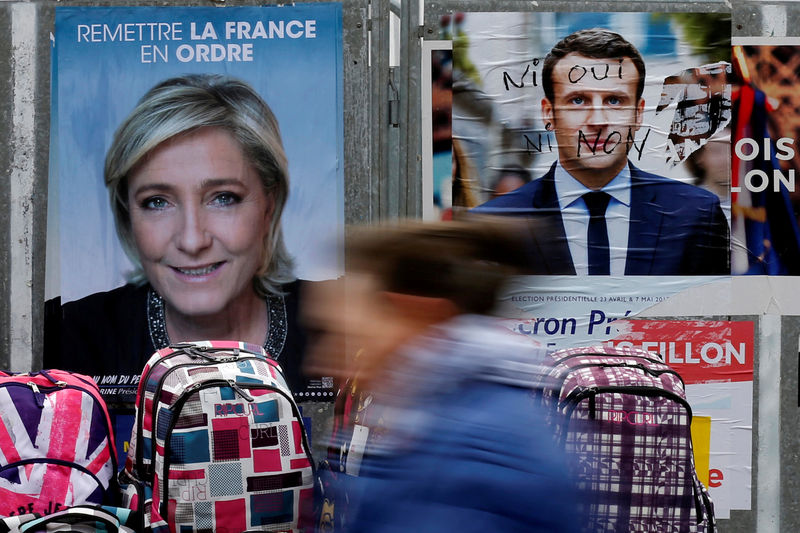 © Reuters. A woman walks past official posters of candidates for the 2017 French presidential election Marine Le Pen and Emmanuel Macron at a local market in Bethune