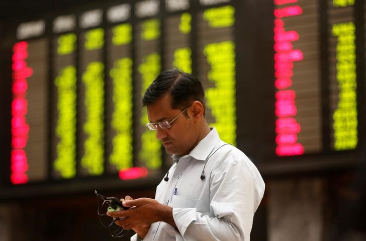 © Reuters. A man uses his cell phone as he stands in front of display board showing stock prices during a trading session in the halls of Pakistan Stock Exchange (PSE) Karachi