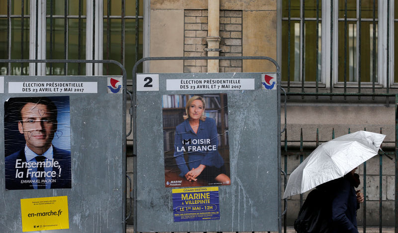 © Reuters. A woman walks past the new official posters of candidates for the 2017 French presidential election Emmanuel Macron, head of the political movement En Marche !, or Onwards !,  and Marine Le Pen, French National Front (FN) political party leader, in Paris