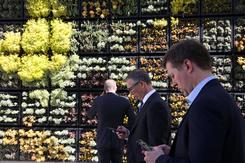 © Reuters. Attendees look at their cellphones in front of a wall garden during the Milken Institute Global Conference in Beverly Hills