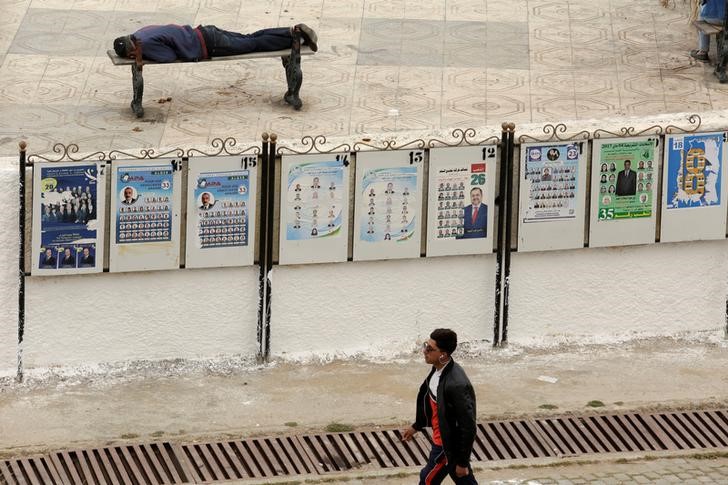 © Reuters. A man walks past campaign election posters in Algiers in Algeria