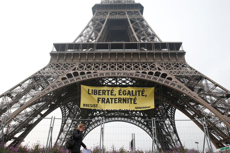 © Reuters. Uma mulher passa pela Torre Eiffel enquanto ativistas do Greenpeace abrem um faixa gigante com mensagem política no monumento, em Paris