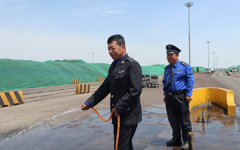 © Reuters. A security guard sprays water onto a road near piles of stored coal at the security check in the port of Tianjin