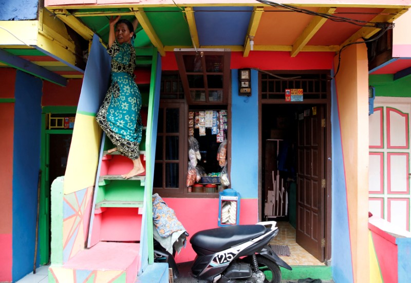 © Reuters. FILE PHOTO: A woman climbs down the stairs of her dwelling located in poor riverside neighborhood where locals have recently painted their homes in bright colours to promote a smoke-free environment in Penas Tanggul, East Jakarta