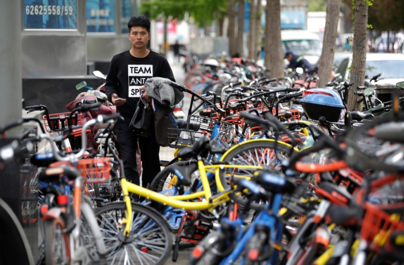 © Reuters. A man looks for a shared bike to ride outside an office building in Beijing