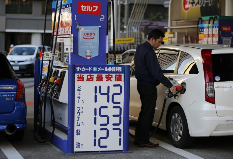 © Reuters. A man refuels a vehicle next to a pricing quotation board at a petrol station in Tokyo