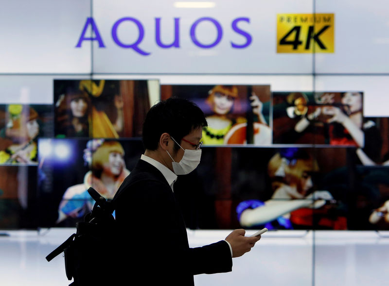 © Reuters. FILE PHOTO: A man using his mobile phone walks past Sharp Corp's liquid crystal display monitors showing the company's Aquos television in Tokyo