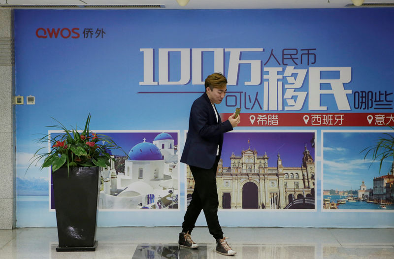 © Reuters. FILE PHOTO: A man stands next to a poster of immigration agency Qiaowai Group at the lobby to its office, in Beijing