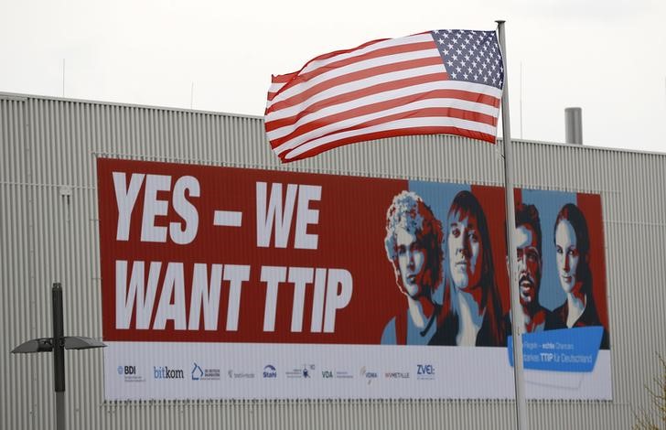 © Reuters. The flag of the USA flutters over a hall of the Hanover Fair decorated with a banner supporting the free trade agreement TTIP in Hanover