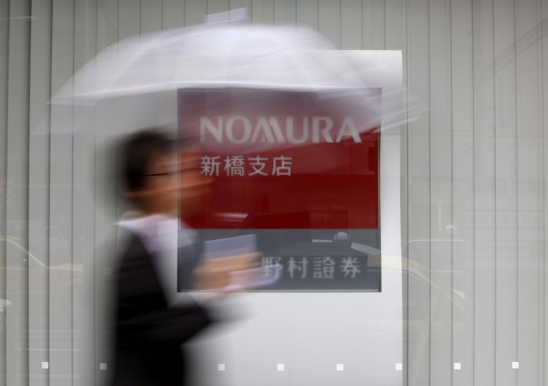 © Reuters. FILE PHOTO: A man holding an umbrella walks in front of a signboard of Nomura Securities outside its branch in Tokyo