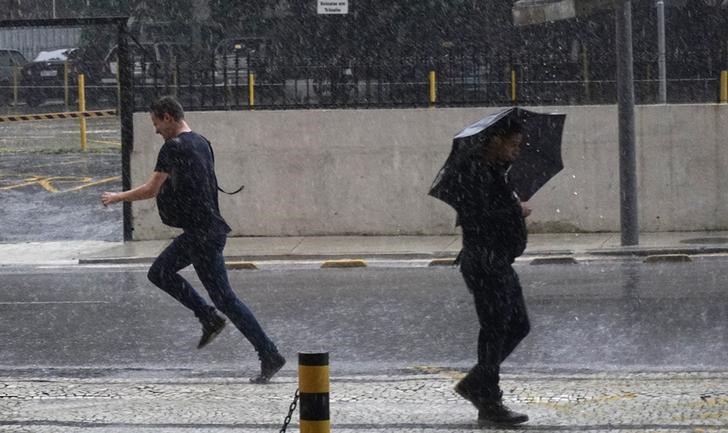 © Reuters. Pessoas tentam se proteger de chuva no Rio de Janeiro