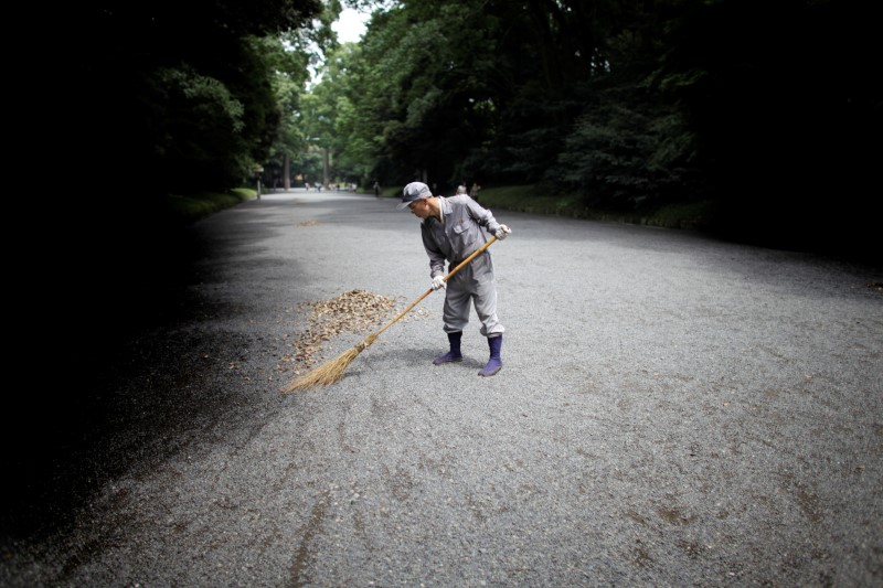 © Reuters. FILE PHOTO: A man sweeps the ground at a temple in Tokyo