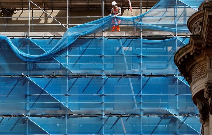 © Reuters. A worker hangs netting from scaffolding on a construction site in Manchester