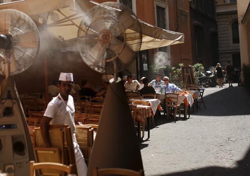 © Reuters. People sit in a restaurant as fans disperse mist during a hot summer day in in Rome