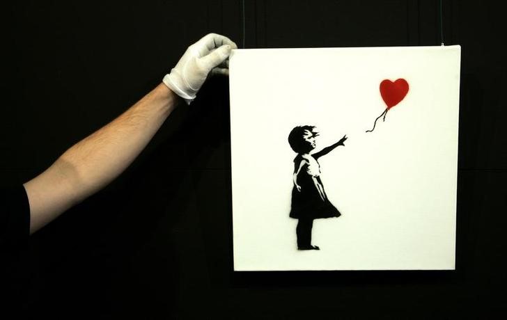 © Reuters. Um técnico de galeria ajusta a obra de arte de Banksy "Balloon Girl" (1975) na casa de leilões da Sotheby's em Olympia, em Londres.