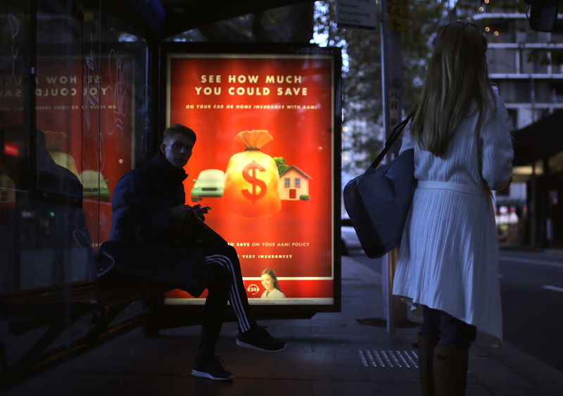 © Reuters. Members of the public wait at a bus stop as an illuminated financial advertisement adorns the bus shelter in central Sydney