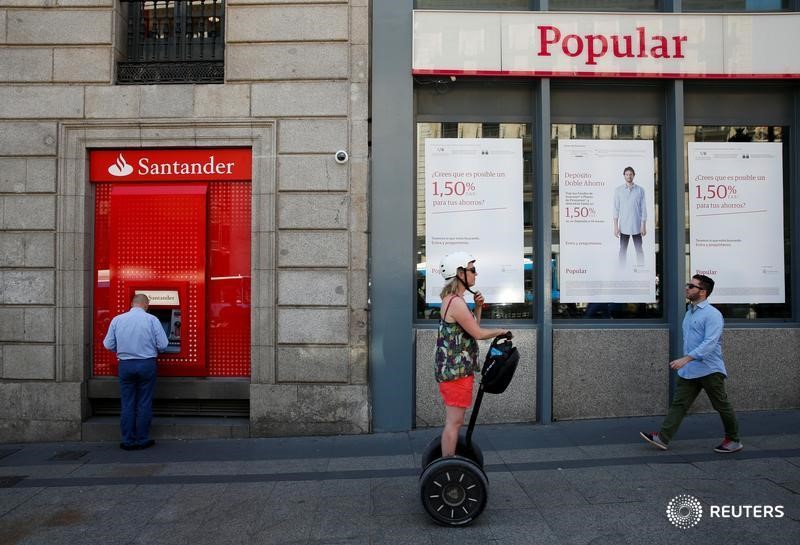 © Reuters. A man uses a cash dispenser at a Santander branch next to a Banco Popular branch in Madrid