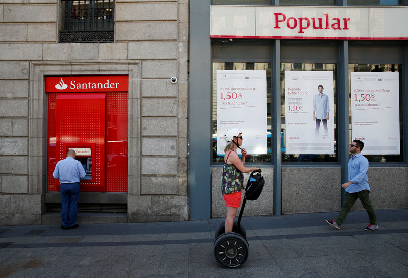 © Reuters. A man uses a cash dispenser at a Santander branch next to a Banco Popular branch in Madrid