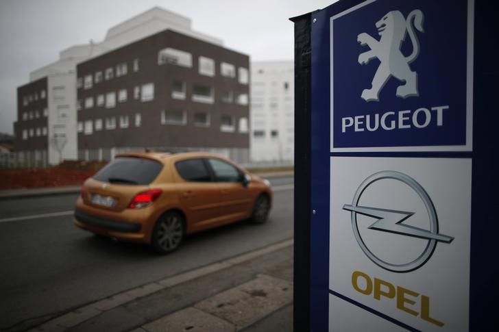 © Reuters. A Peugeot car drives past the logos of French car maker Peugeot and German car maker Opel at a dealership in Villepinte