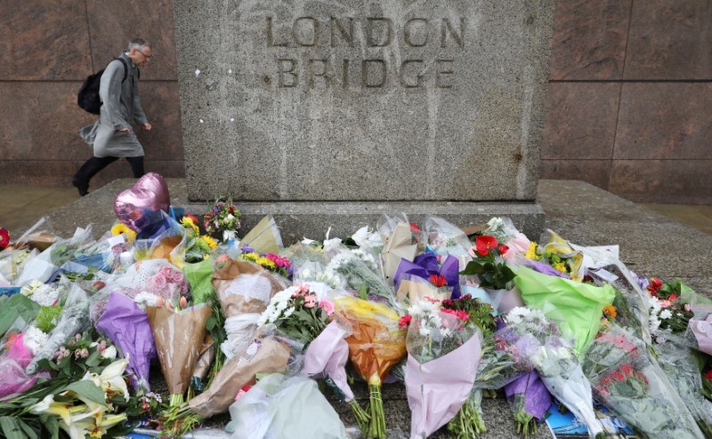 © Reuters. FILE PHOTO: A man walks past flowers and tributes left for the victims of the attack on London Bridge and Borough Market on a wet and windy morning in London