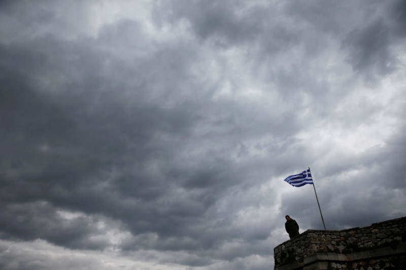 © Reuters. FILE PHOTO: A man looks down as a Greek national flag flutters atop one of the bastions of the 17th century fortress of Palamidi under an overcast sky at the southern port city of Nafplio