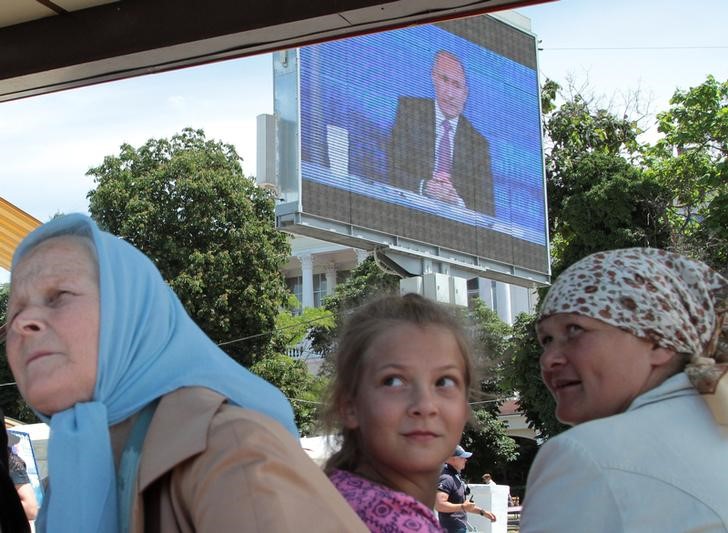 © Reuters. Люди на фоне экрана, транслирующего прямую линию с президентом РФ Владимиром Путиным, в Севастополе