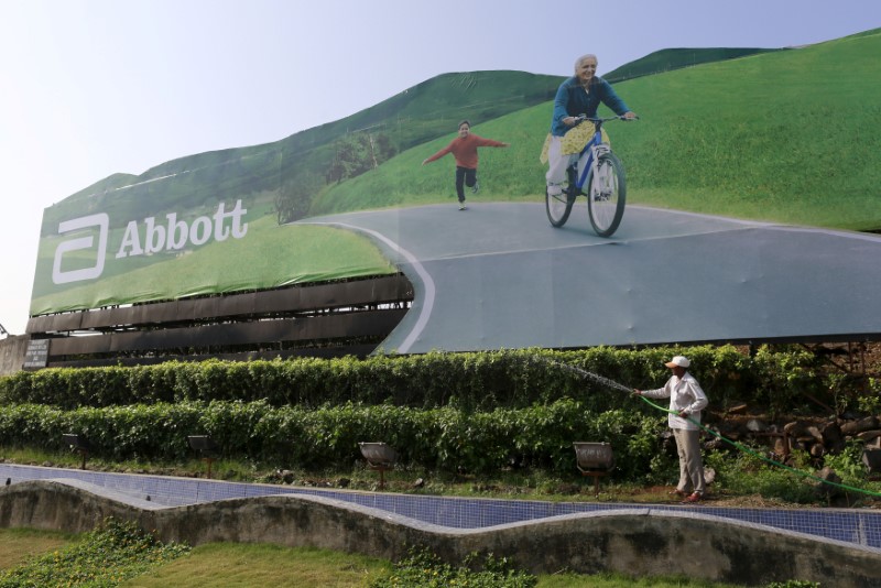© Reuters. FILE PHOTO: A worker waters plants next to an advertisement billboard of Abbott in Mumbai