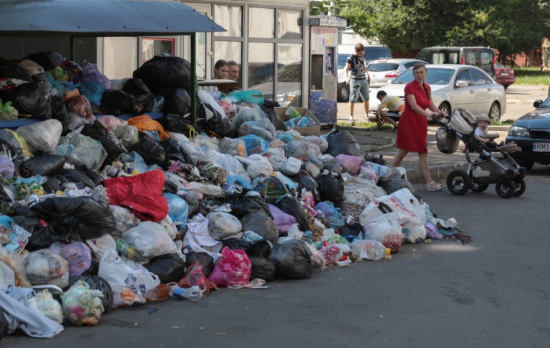 © Reuters. A woman pushes a child in a stroller past a pile of trash in Lviv