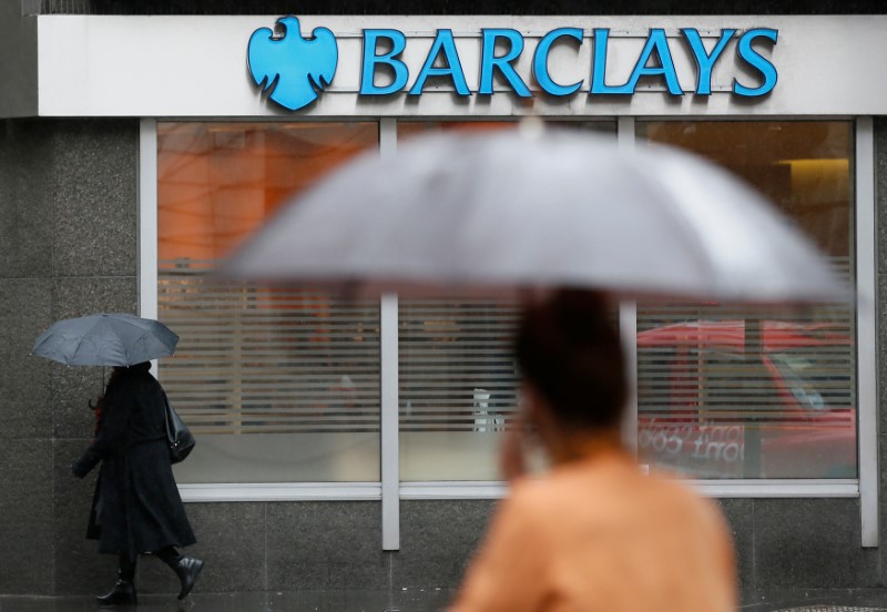 © Reuters. FILE PHOTO: Pedestrians shelter under umbrellas as they walk past a Barclays branch in central London