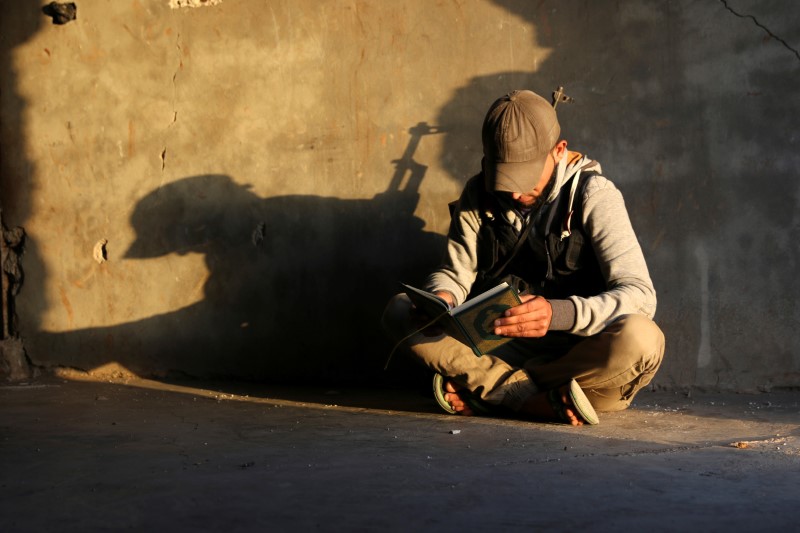 © Reuters. A Free Syrian Army fighter reads the Koran before Iftar during the Muslim month of Ramadan in the province of Daraa, Syria