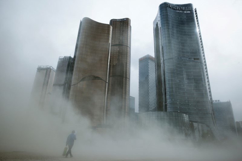 © Reuters. FILE PHOTO: A man walks through a cloud of dust whipped up by wind at the construction site near newly erected office skyscrapers in Beijing
