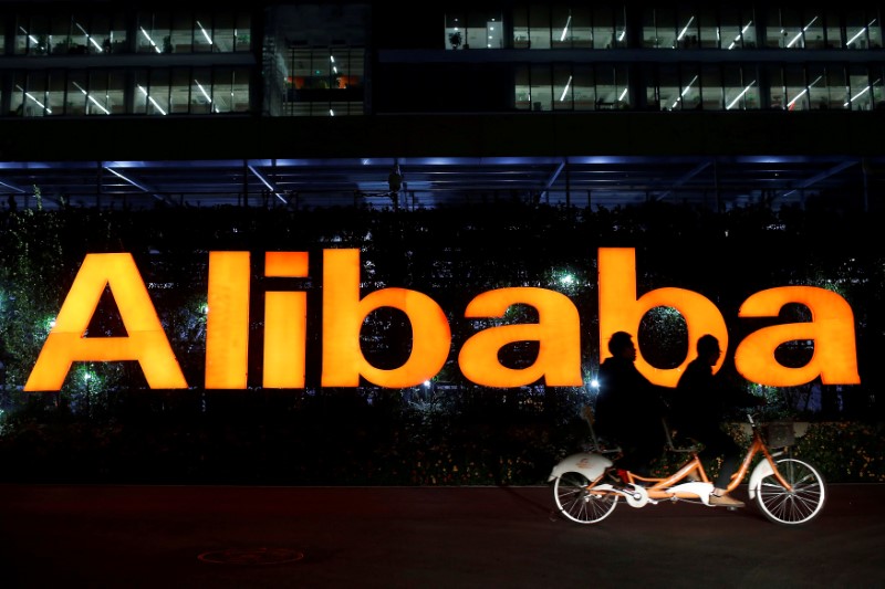 © Reuters. FILE PHOTO: People ride double bicycle past Alibaba Group logo at the company's HQ on the outskirts of Hangzhou